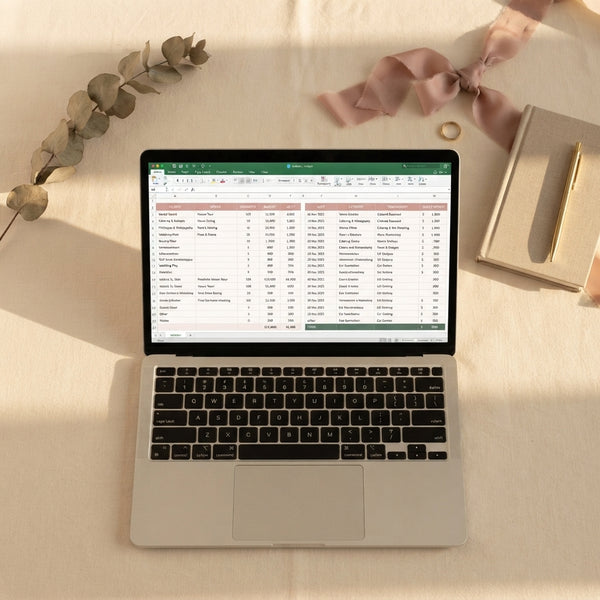 Laptop displaying a digital wedding budget spreadsheet on a desk with silk ribbon and eucalyptus, styled in warm tones.
